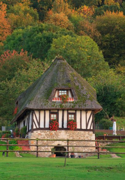 Maison traditionnelle à colombages avec toit de chaume, entourée de nature automnale et de verdure paisible